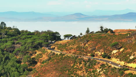 Dia--Und-Schwenkaufnahmen-Von-Autos,-Die-Auf-Der-Straße-Auf-Dem-Land-Vorbeifahren.-Bergrücken-Und-Nebelüberflutetes-Tal-Im-Hintergrund.-Kapstadt,-Süd-Afrika