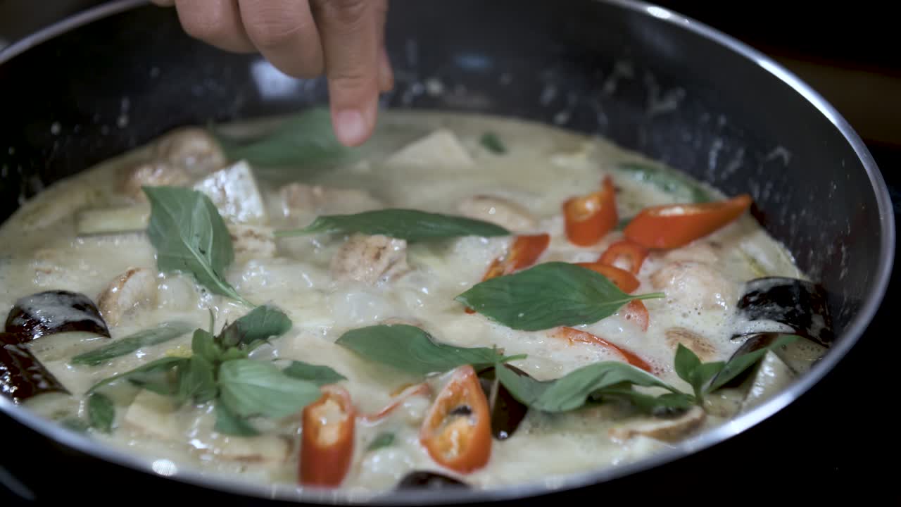 Thêm húng quế Thái tươi vào món cà ri rau củ thuần chay lành mạnh đang sôi nhỏ lửa trong chảo đen