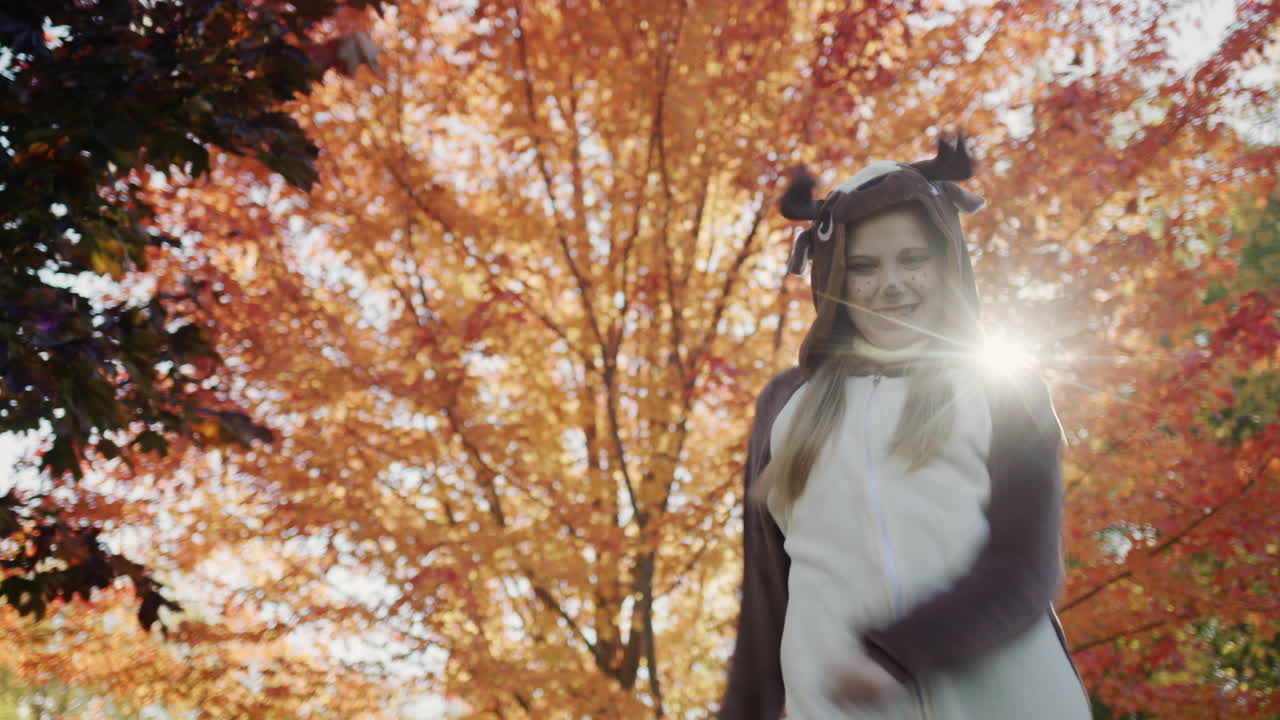 un niño en un disfraz de ciervo baila cerca de un árbol de otoño