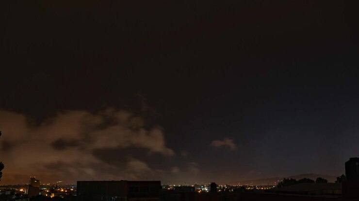 Lyn slår ned bag en mørk bysilhuet under tunge stormskyer om natten, time-lapse af takkede lyn.