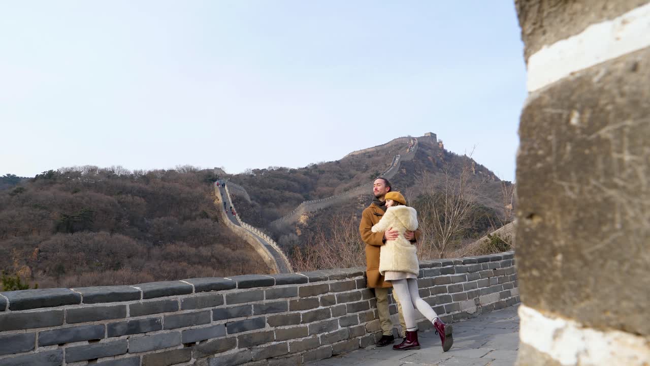 Young couple standing observing the views of the mountains from the Great Wall of China in winter, eye level shot of couple kissing and cuddling romantic