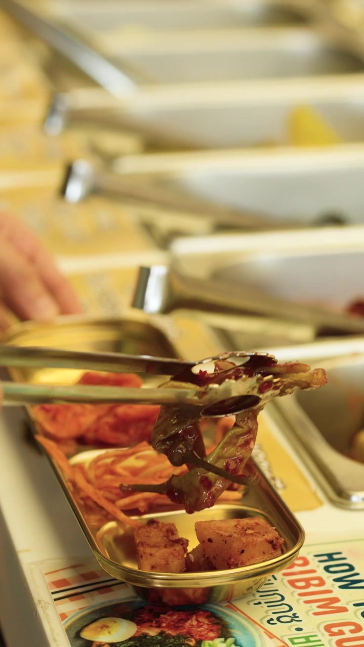 Primo piano di una mano che sistema vari contorni coreani in un vassoio di metallo in un ristorante.