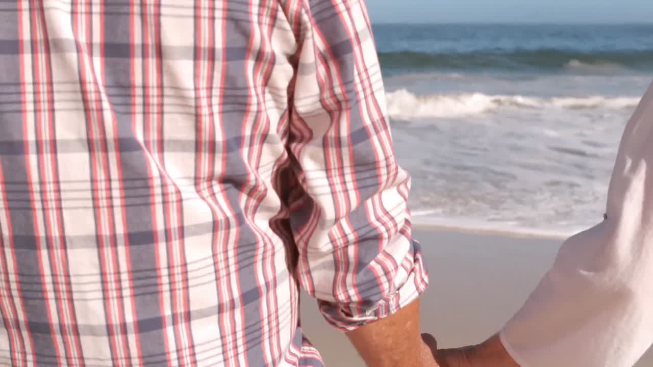 una pareja de ancianos tomados de la mano en la playa.