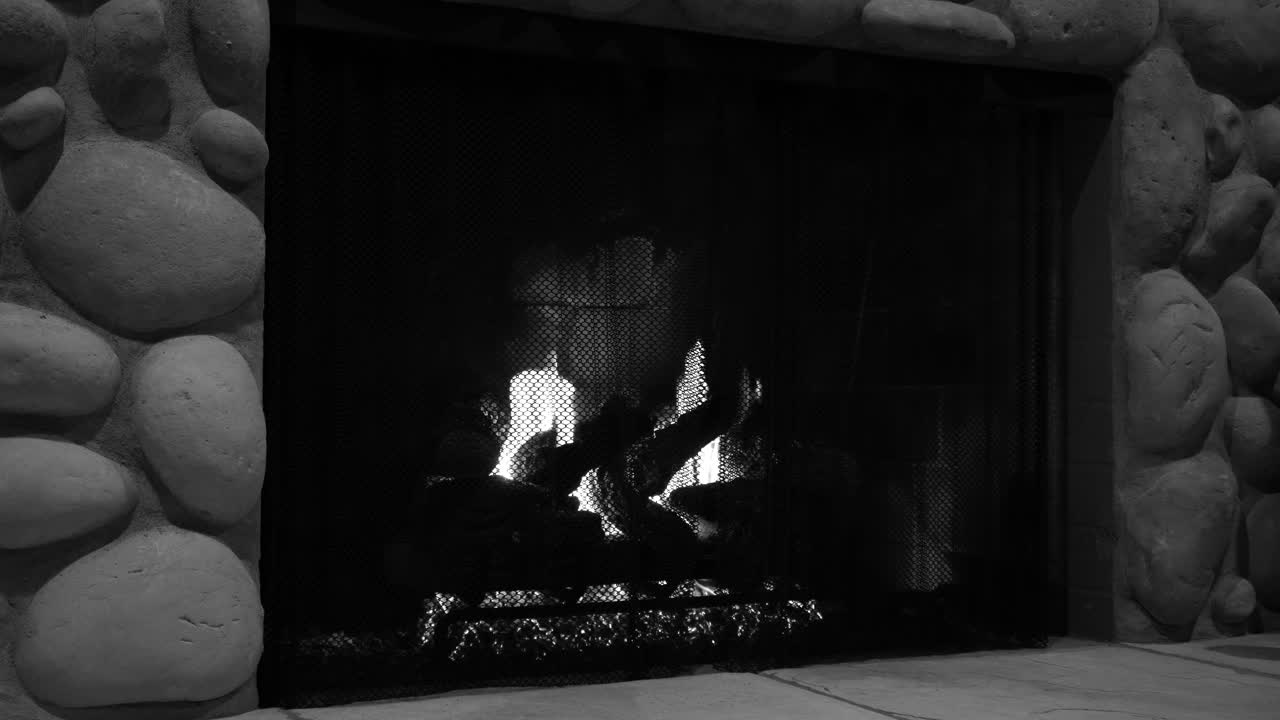 Black and white fire burns in a stone fireplace film noir still shot