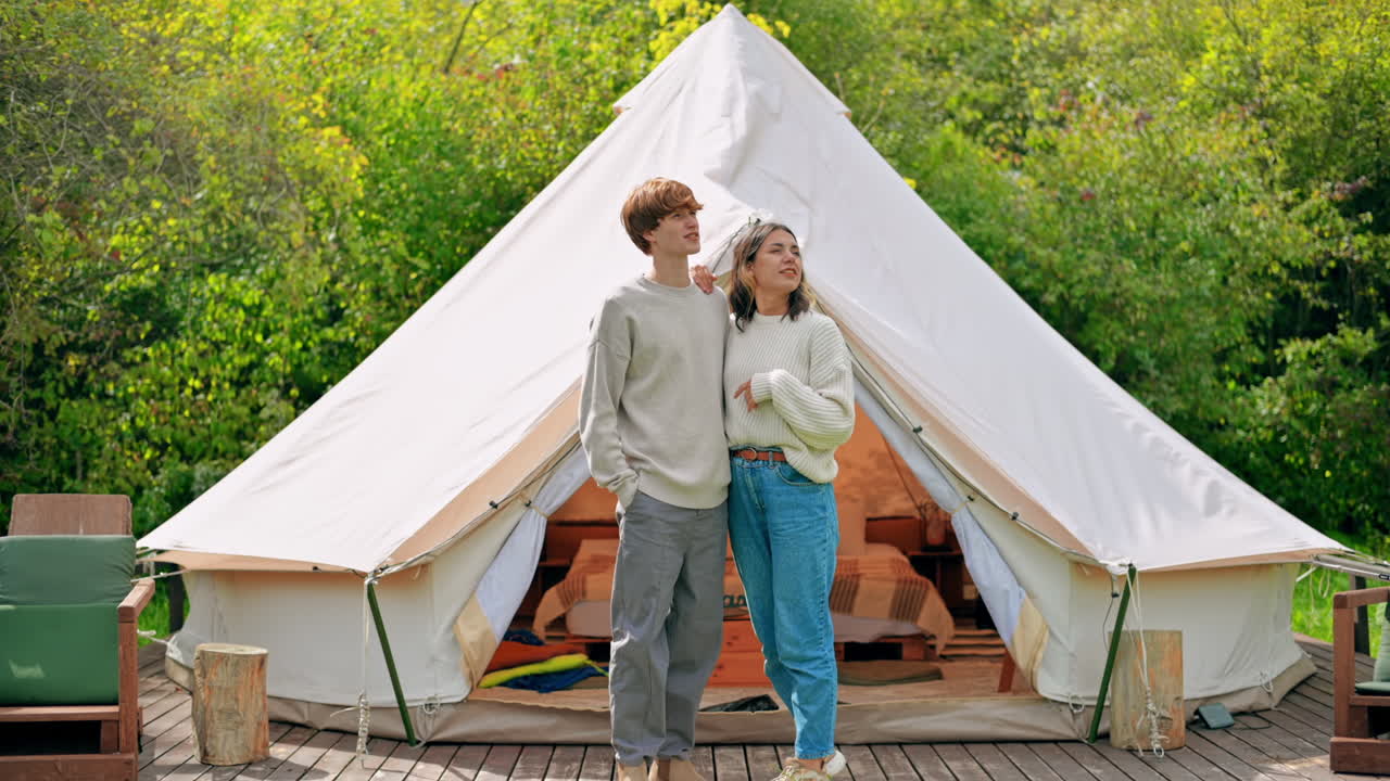 Una coppia che si abbraccia e parla sulla terrazza di una tenda in un glamping. Rigogliosa foresta circostante