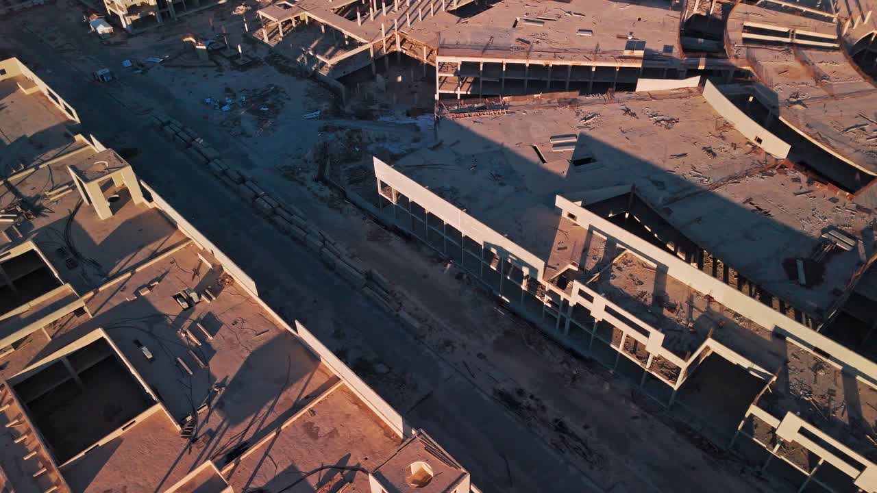Ripresa aerea cinematografica 4K con drone di un complesso in cemento incompiuto con cortili, aperture sul tetto, detriti e lunghe ombre durante l'ora d'oro, ideale per contenuti visivi di sviluppo e immobiliari