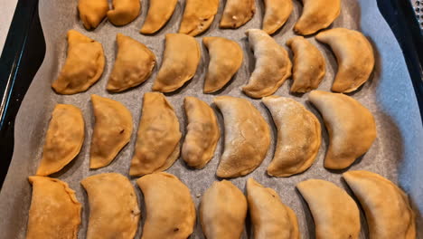 tray of neatly arranged uncooked dumplings lined on baking paper ready for the oven