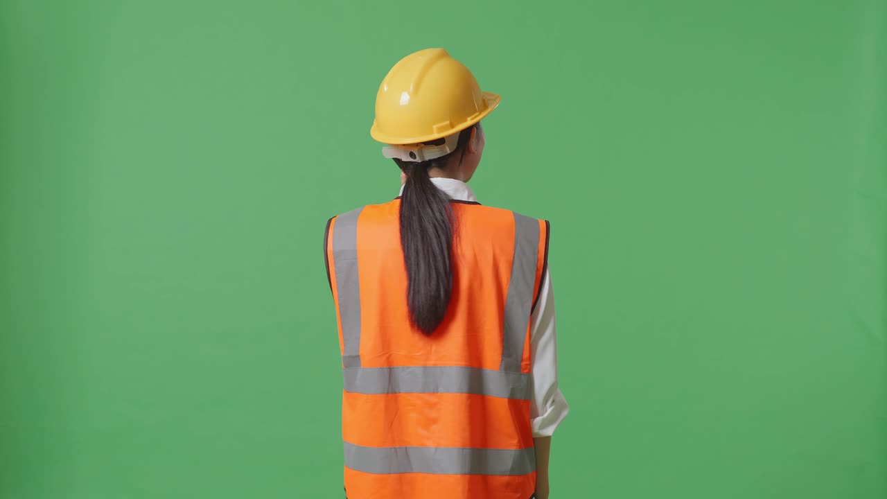 안전 헬을 입은 아시아 여성 엔지니어가 녹색 화면 배경 스튜디오에 서서 스마트폰으로 대화하는 모습