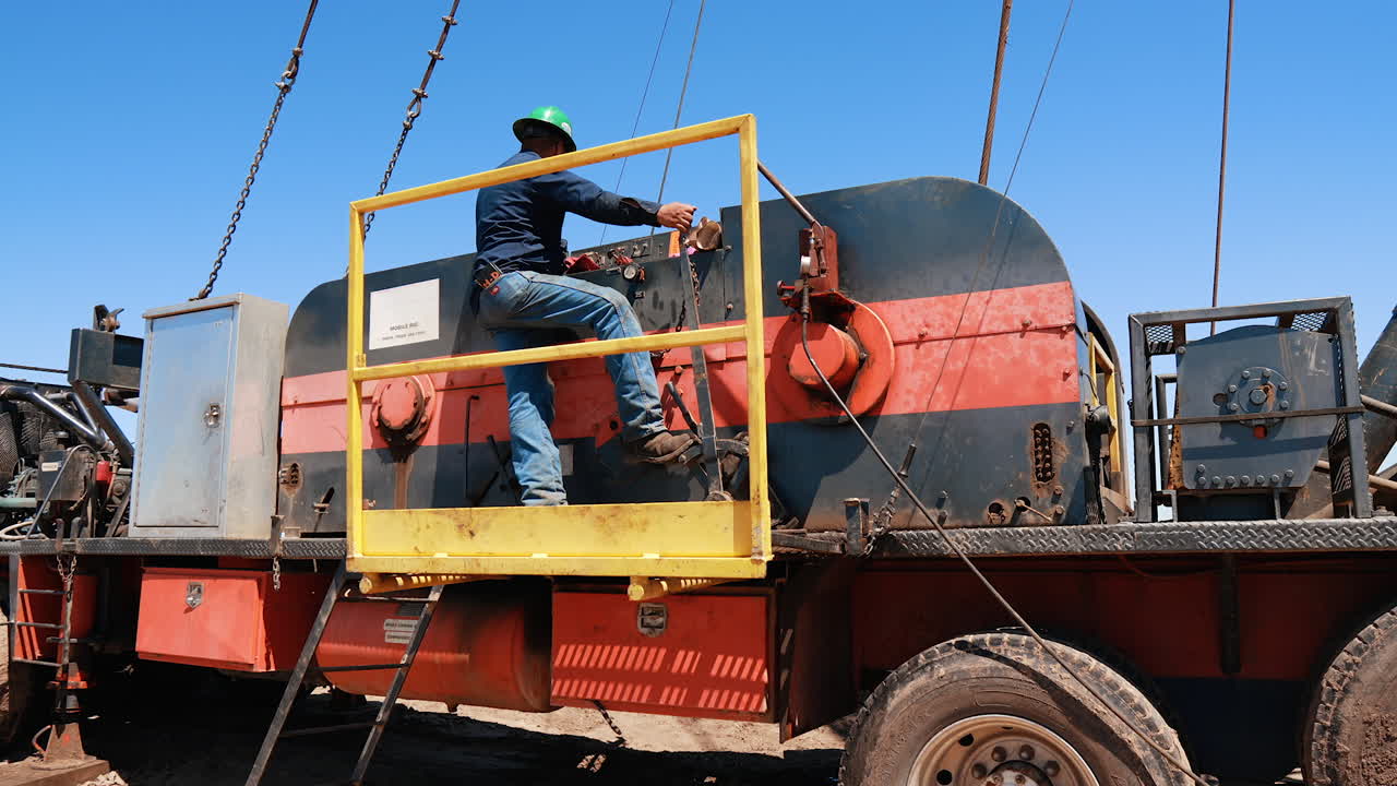 Man in helmet standing at deck of a truck with boring equipment. Rear view of an engineer operating drilling equipment.