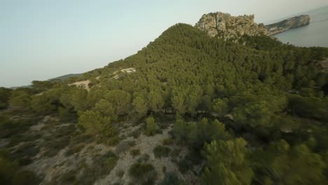 FPV-drone-forward-moving-shot-flying-low-over-hilly-terrain-along-the-Cala-d'egos-beach,-Mallorca,-Spain-during-evening-time