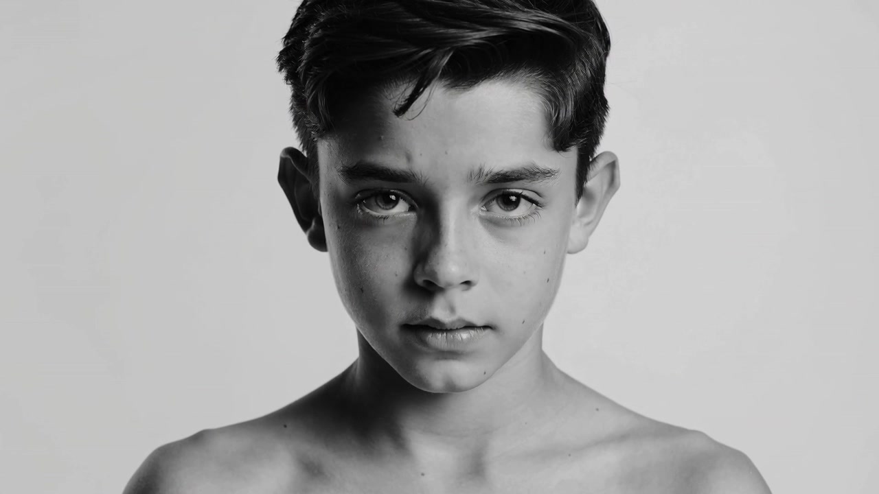 Adolescente sem camisa de frente mantendo o olhar em retrato enquanto a câmera começa com um fundo simples e luzes.
