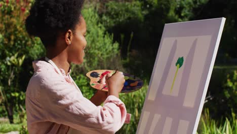 mulher afro-americana sorridente pintando uma imagem em tela em um jardim ensolarado