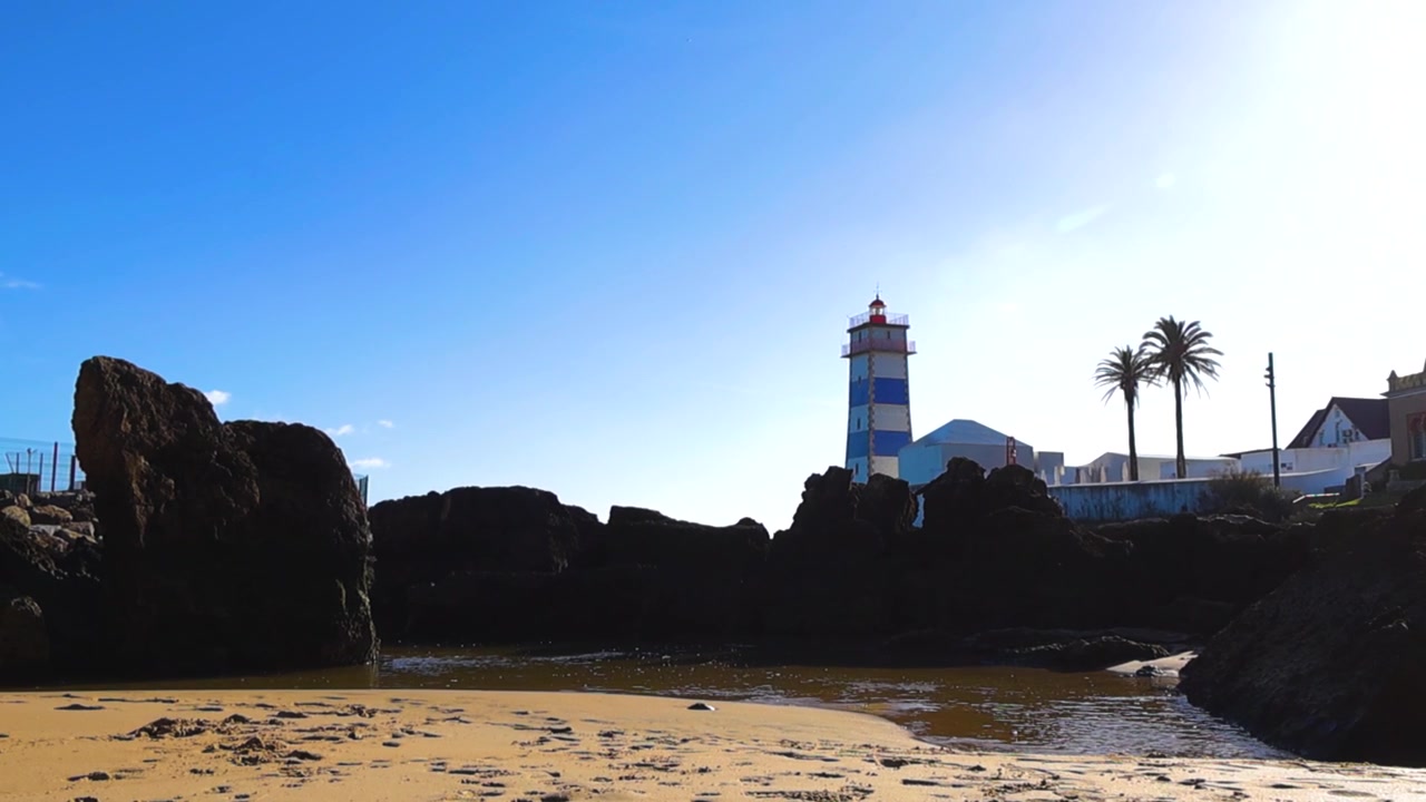 Beautiful view of the Santa Marta lighthouse and museum in Cascais, Portugal, with a small rocky beach in the foreground on a bright sunny day against a clear blue sky