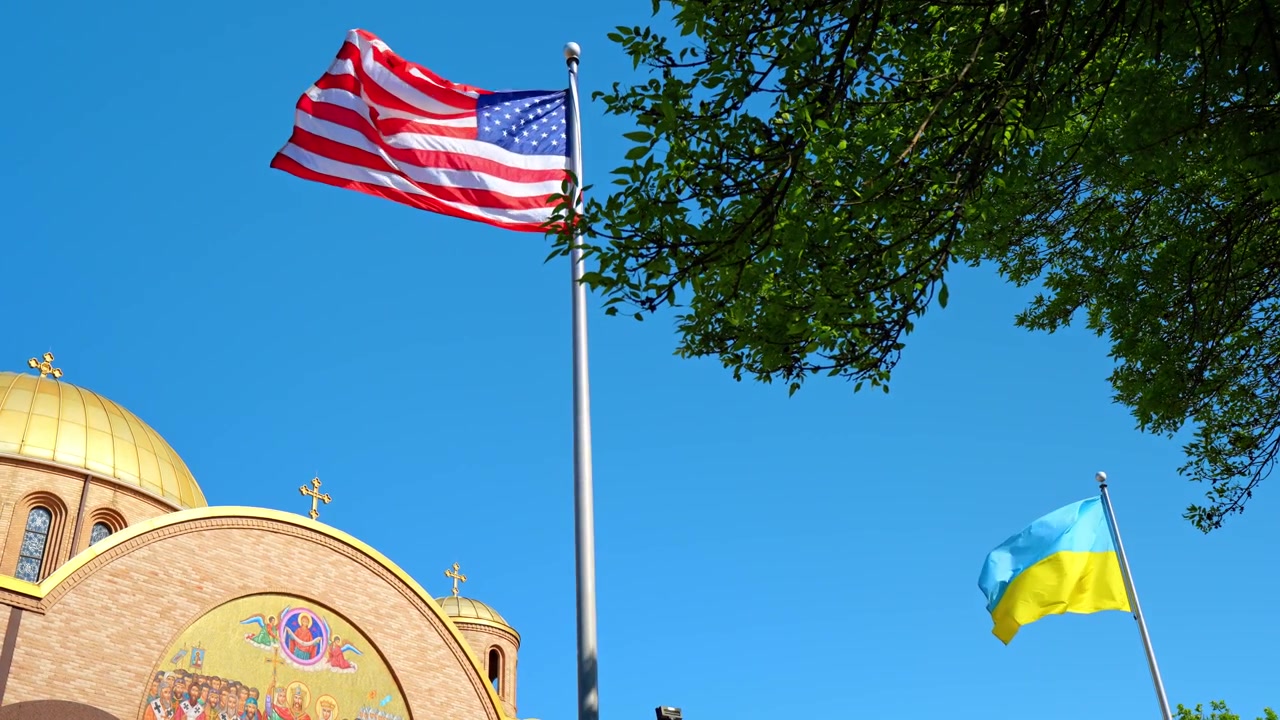 American and Ukrainian flags flying near orthodox cathedral, Chicago. Low angle view of gold domed church with mosaic and flags against clear sky.