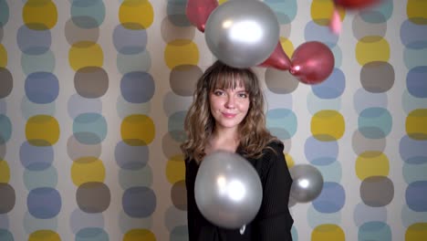 mujer joven parada frente a globos flotantes en el aire contra un fondo colorido