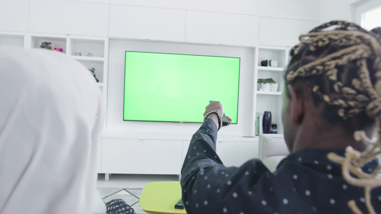 Green screen tv with african couple on sofa at home rear view