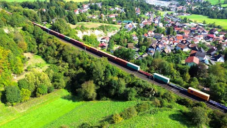 Drone-Aéreo-Sobre-Un-Tren-De-Carga-Que-Pasa-Por-Un-Pueblo-Rural-4k