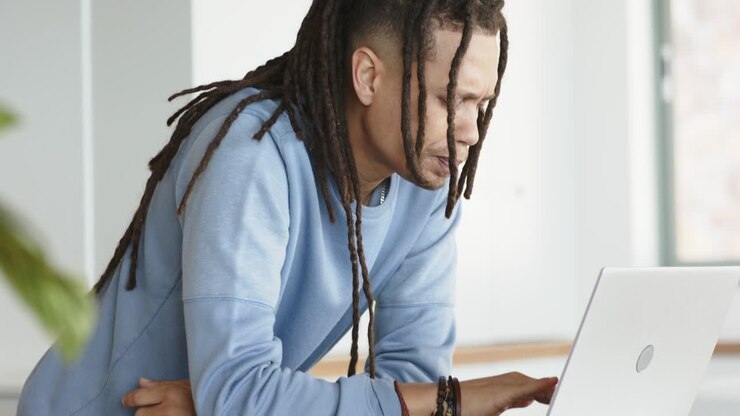 Mid adult African American man studying laptop screen on desk typing while focusing at home office