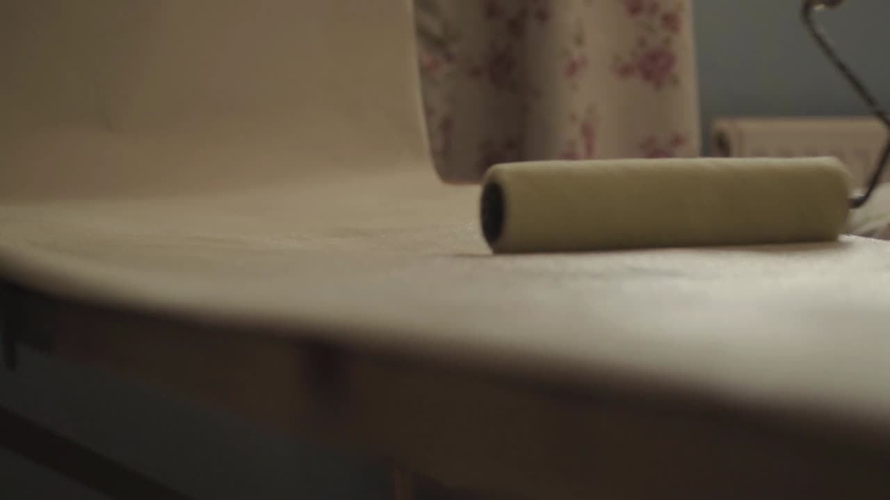 Man decorator using roller to apply adhesive paste on roll of wallpaper