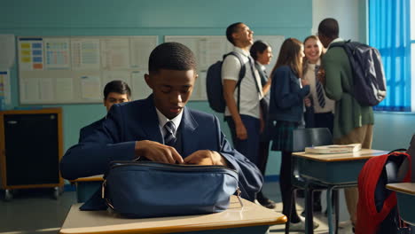 student in uniform putting a book into a bag in a classroom