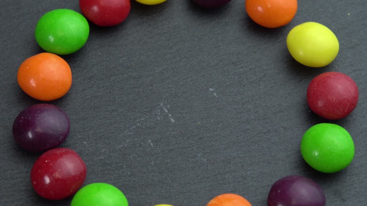 los dulces de colores giran sobre un fondo negro y la mano toma un dulce, dulces de color