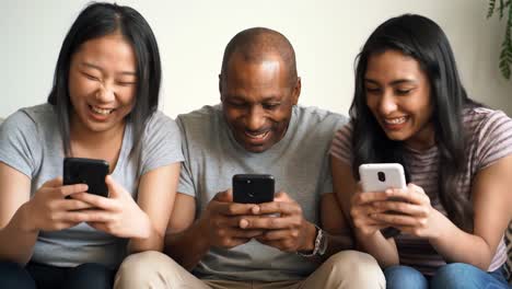 three friends engaged in lively conversation and laughter while using their smartphones in a cozy indoor setting