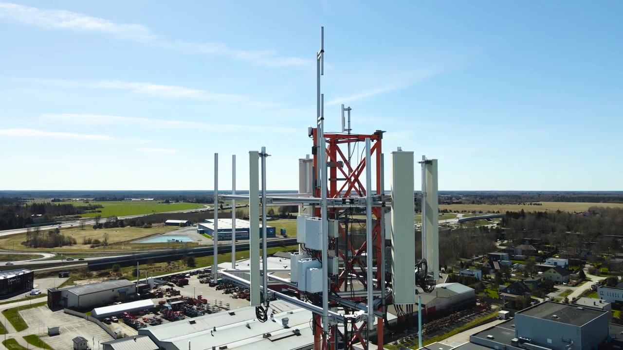 Ripresa aerea con drone che circonda una torre di trasmissione cellulare equipaggiata con antenne 5G e 6G per la rete mobile, che trasmette internet ad alta velocità e segnali di comunicazione su una vasta area urbana