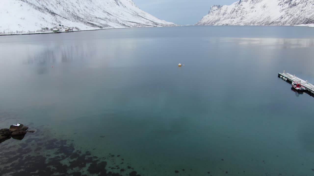 Drone view in Tromso area in winter flying over a fjord surrounded by white snowy mountains and pebble beach in Norway