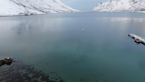 vista del avión no tripulado en el área de tromso en invierno volando sobre un fiordo rodeado de montañas blancas nevadas y playa de guijarros en noruega