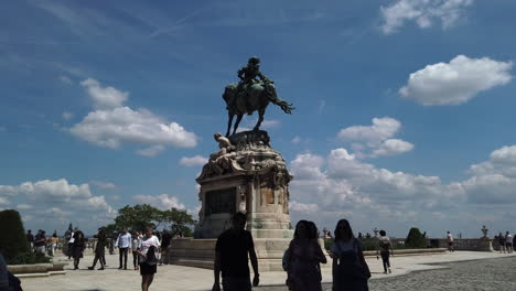 4k statue of prince eugene of savoy. the statue is at the centre of the scene. a blue sky full white clouds are in the background. people walk and take pictures around the statue.