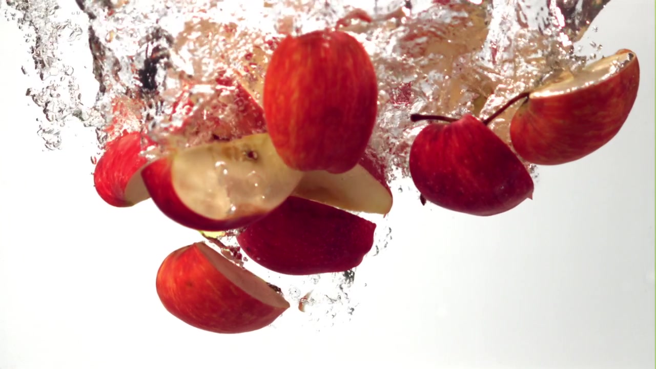 Fette di mela rossa che cadono e schizzano nell'acqua limpida.