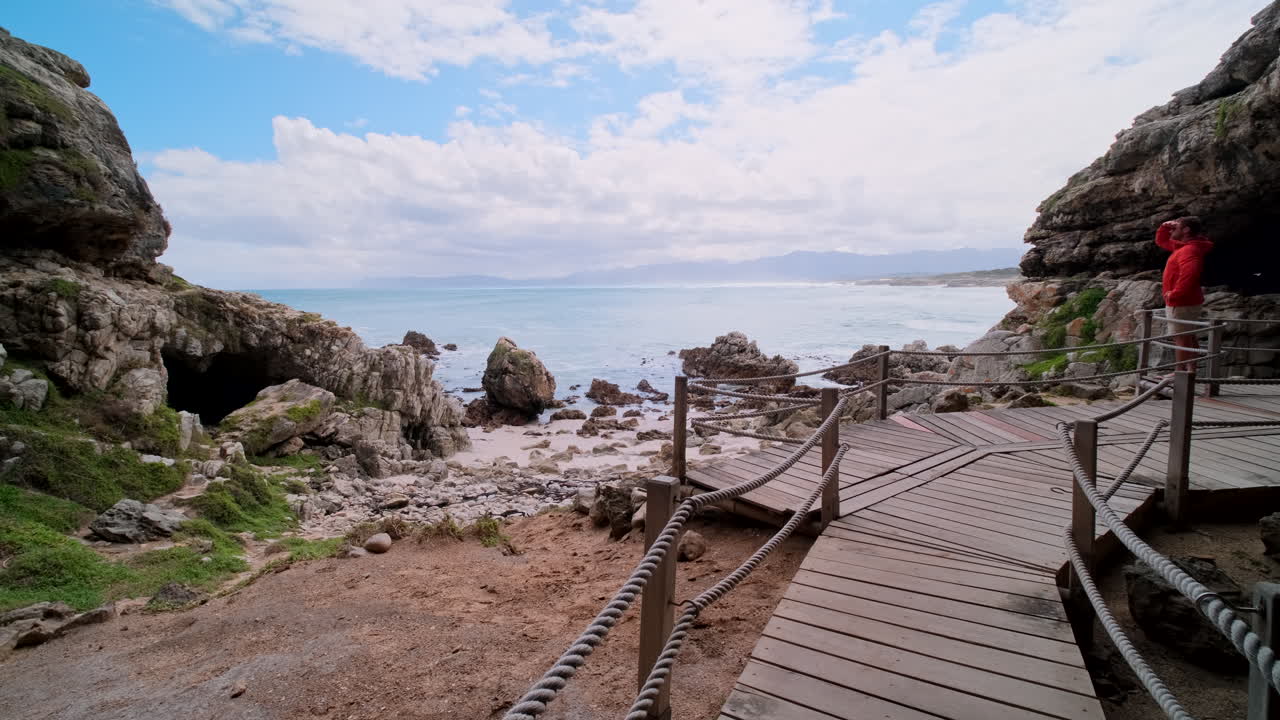 Male traveler explores historic Klipgat Cave on wooden walkway overlooking ocean