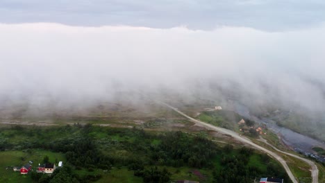 clouds and fog above the nordic village surrounded by green forest in norway