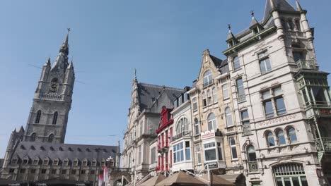 iconic view of the belfry of ghent and surrounding historic buildings in sint-baafsplein square, belgium, featuring ornate facades and clear blue skies.