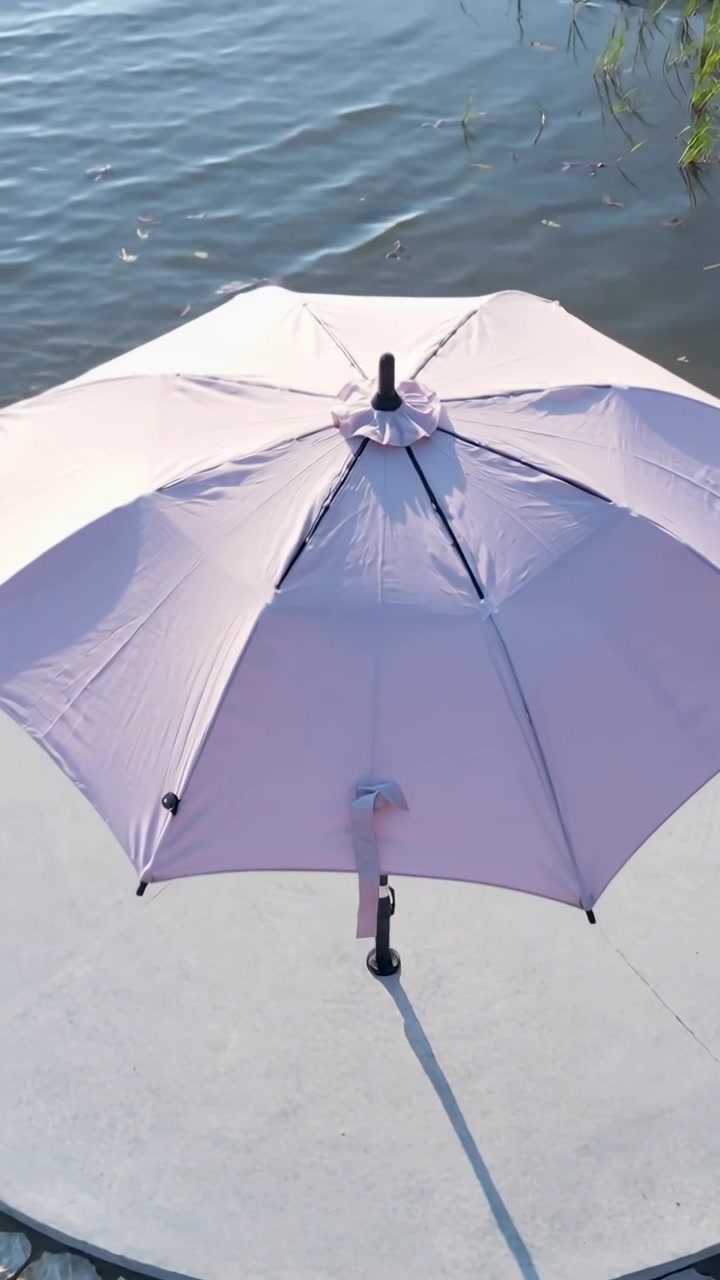 Video verticale: La telecamera panoramica rivela un ombrellone rosa su una lastra di cemento vicino all'acqua, con una barca che entra.
