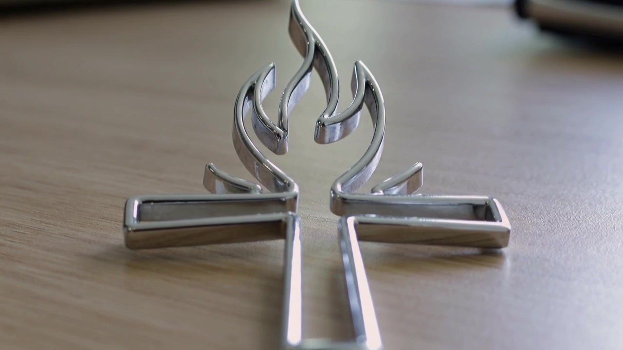 Telecamera che si avvicina a un emblema d'argento lucido su una scrivania di legno, evidenziando un dettaglio a forma di fiamma.