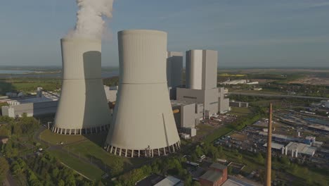 aerial drone view of the lippendorf power plant near leipzig, germany. cooling towers, smoke, and industrial facilities surrounded by green fields under clear sky.