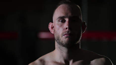 dark lit medium close up of a young male mixed martial artist intensely looking at the camera after a training session