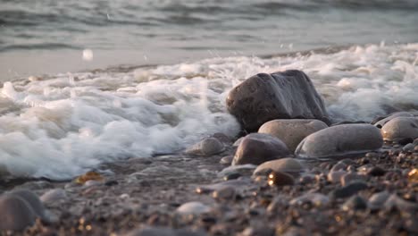 small delicate waves crashing into wet rocks on a beach at sunset. slow motion