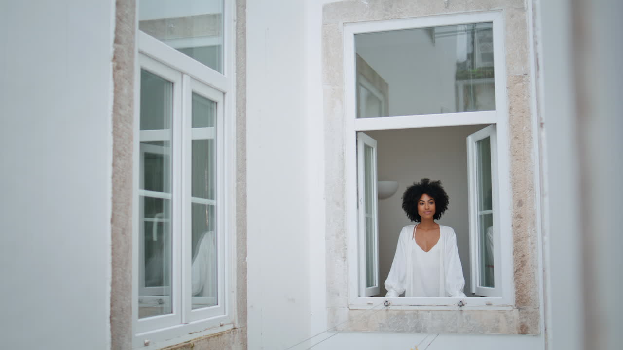 Positive lady looking outdoors at window place. African woman watching cityscape