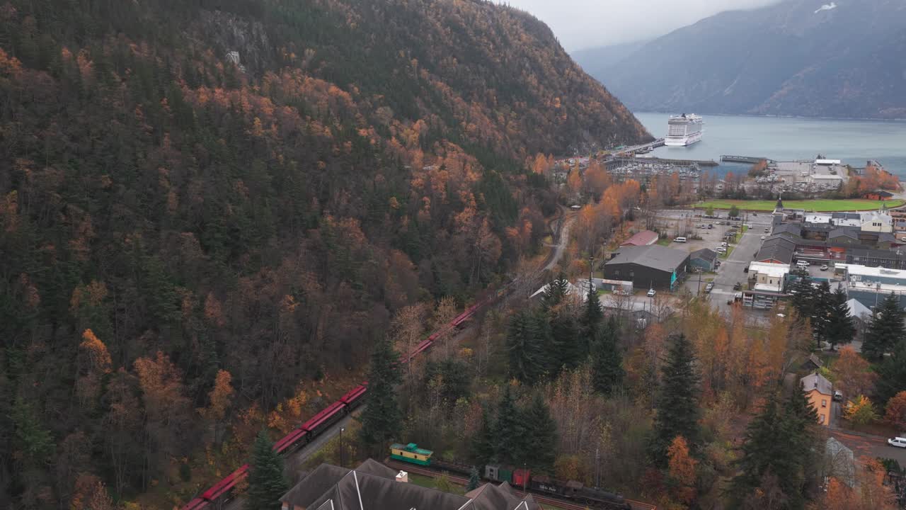 Aerial wide descending shot of the White Pass Yukon Route Railway arriving in Skagway during the fall season in Southeast Alaska. 4K