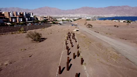 aerial slow backwards drone shot of environmental sculptures lined in rows near the city of eilat, surrounded by desert, sea, and the city