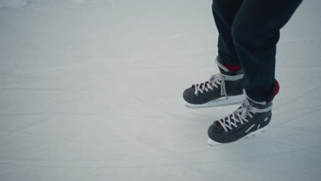close up leg view of skater wearing black trousers and hockey skates gliding across icy rink surface with crisp winter light highlighting skate blades and ice markings during outdoor skating session