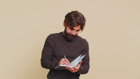 Thoughtful businessman making notes writing down thoughts with pen into diary on beige background