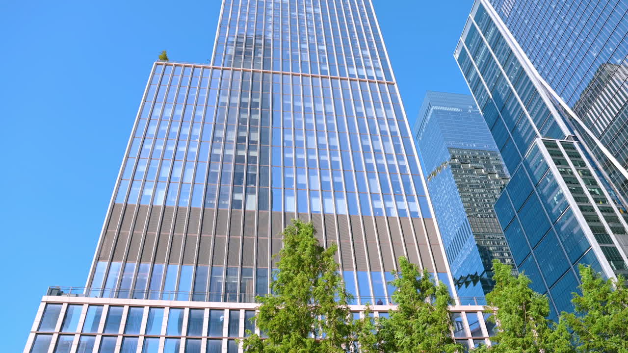 New York, USA, 5 August 2025: High-rise glass buildings of modern New York reflecting blue sky. The Vessel Structure stands nearby. Low angle view