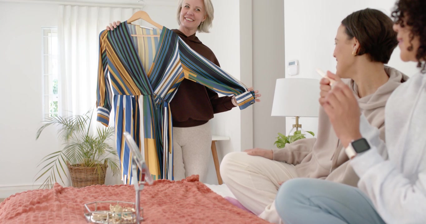 Amiche che guardano una donna di mezza età entrare e mostrare un vestito a righe per chiedere un parere in camera da letto