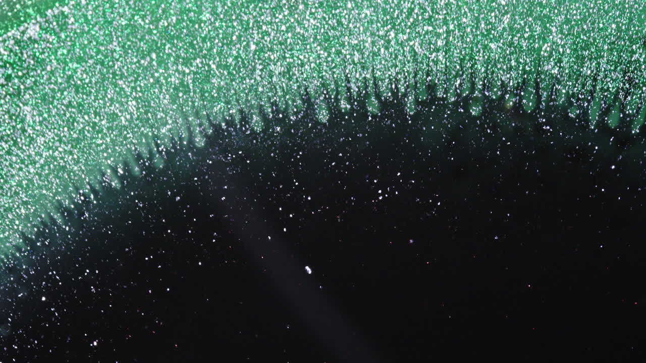 Makroaufnahme von sich vermischender Tinte, die eine glitzernde, abstrakte Textur erzeugt
