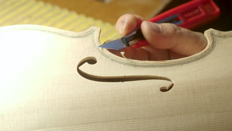 macro-close-up-of-artisan-luthier-maker-work-on-new-classic-handmade-raw-violin-smooth-edge-in-waist-and-purfling-rasp-in-workbench-of-workshop-in-Cremona-Italy-4k-video