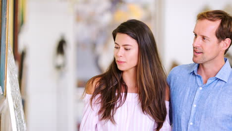 una joven pareja blanca mirando pinturas en una galería de arte.