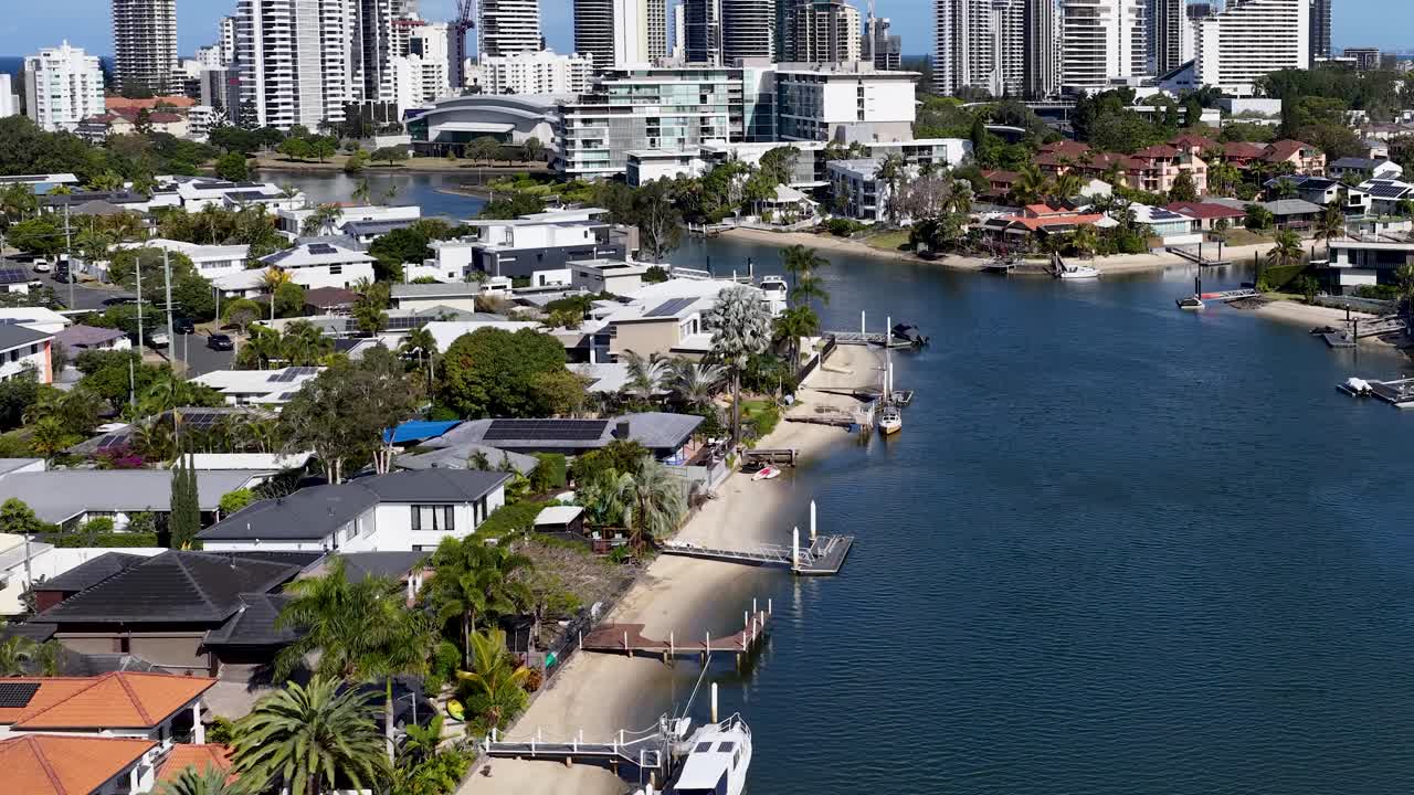 Drone glides above canal, luxury houses, and city skyline in bright midday sunlight